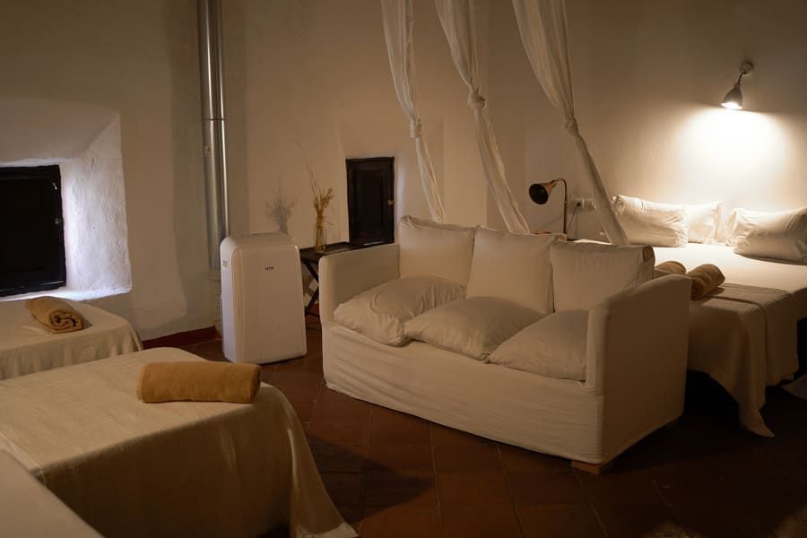 Dormitorio blanco con sofá y dos camas, con luz natural y decoración sencilla.