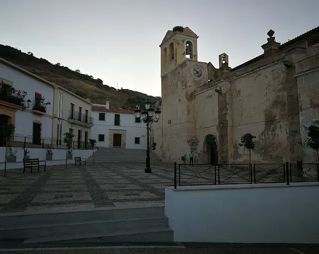 Una plaza con iglesia y edificios. Una plaza de piedra en un pueblo. Montaña al fondo, al anochecer.