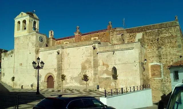 Exterior de la iglesia a la luz del sol: paredes beige, campanario, puerta marrón y cielo azul.