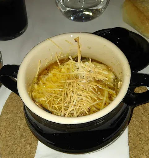 Sopa de cebolla francesa en un tazón negro, cubierta con queso.