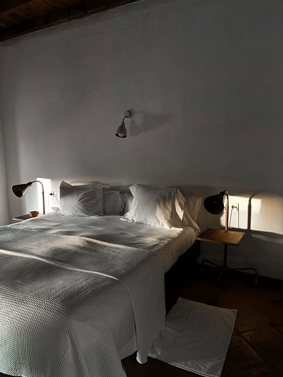 Cama blanca con lámparas a ambos lados, en una habitación luminosa.