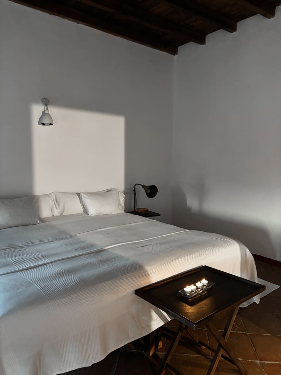 Dormitorio con cama blanca, bandeja con velas y techo con vigas de madera oscura.