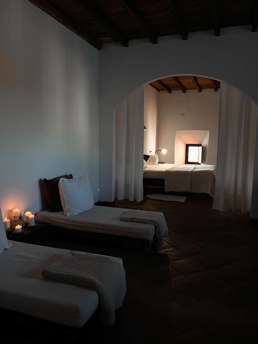 Sala de spa con tumbonas blancas, arco hacia las camas de tratamiento y velas.