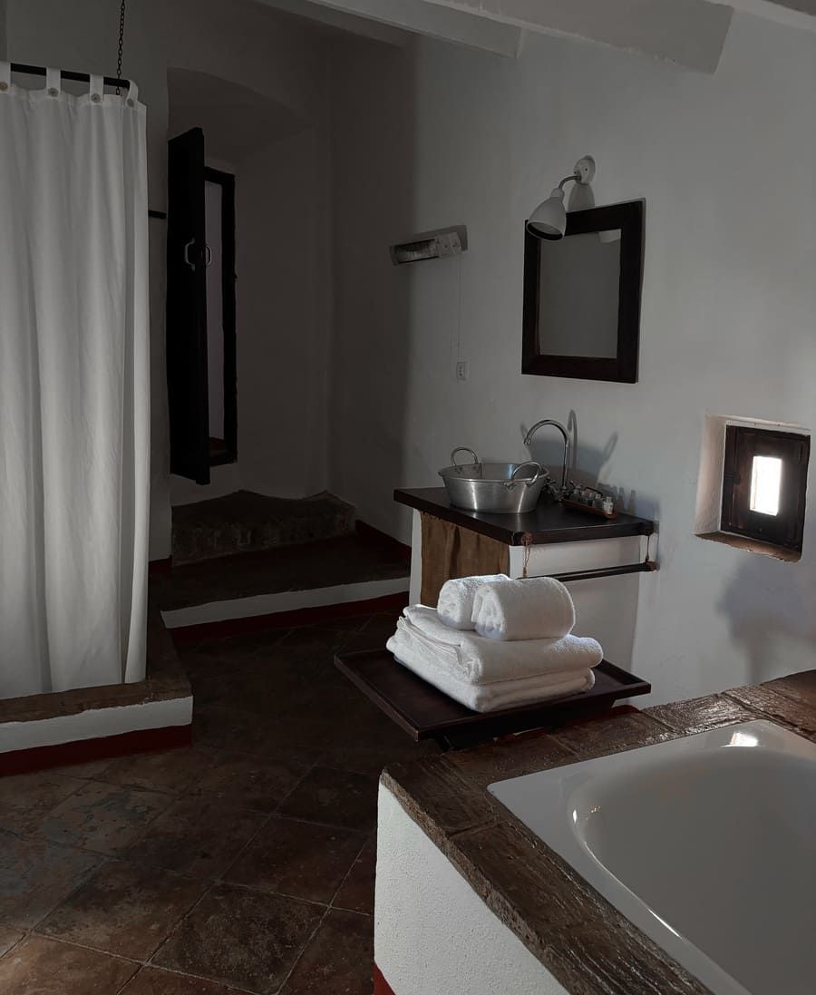 Baño con bañera blanca, toallas, lavabo y ducha. Decoración rústica y oscura.