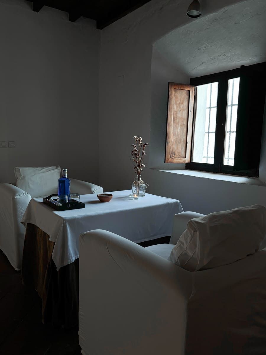 Dos sillas blancas frente a una mesa colocada frente a una ventana. La luz del sol entra a raudales.