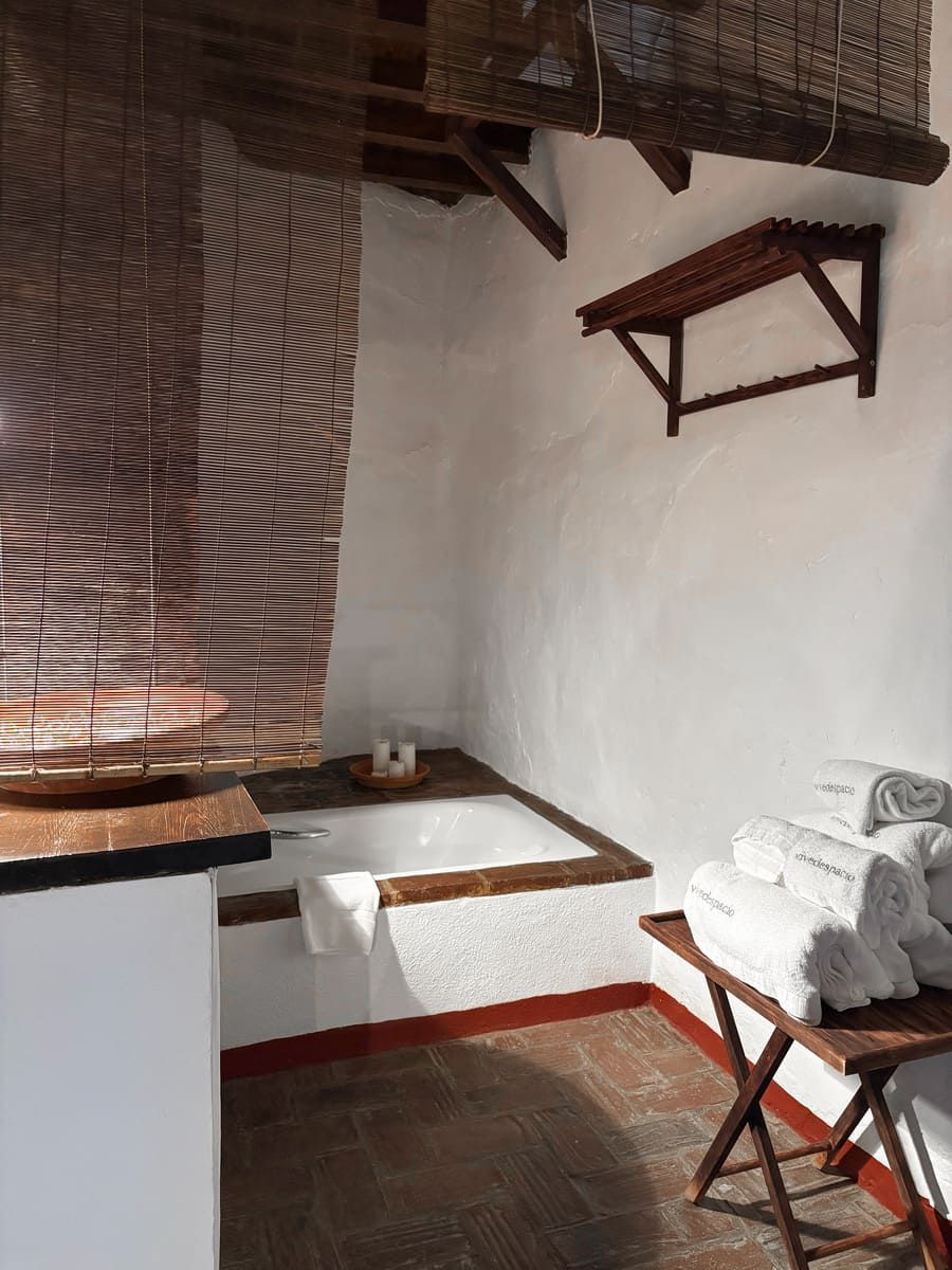 Baño con pared de ladrillo, paredes blancas, bañera y toallas sobre una mesa de madera.