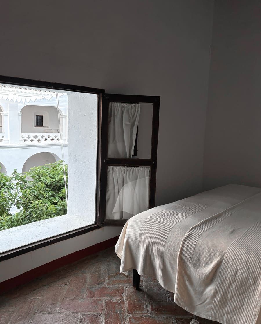 Dormitorio con cama, ventana que da a un patio abovedado con follaje.