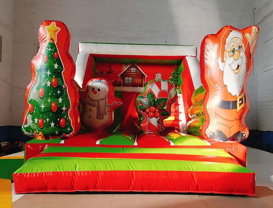 Castillo inflable navideño con Papá Noel, árbol de Navidad y muñeco de nieve. Diseño rojo y verde.