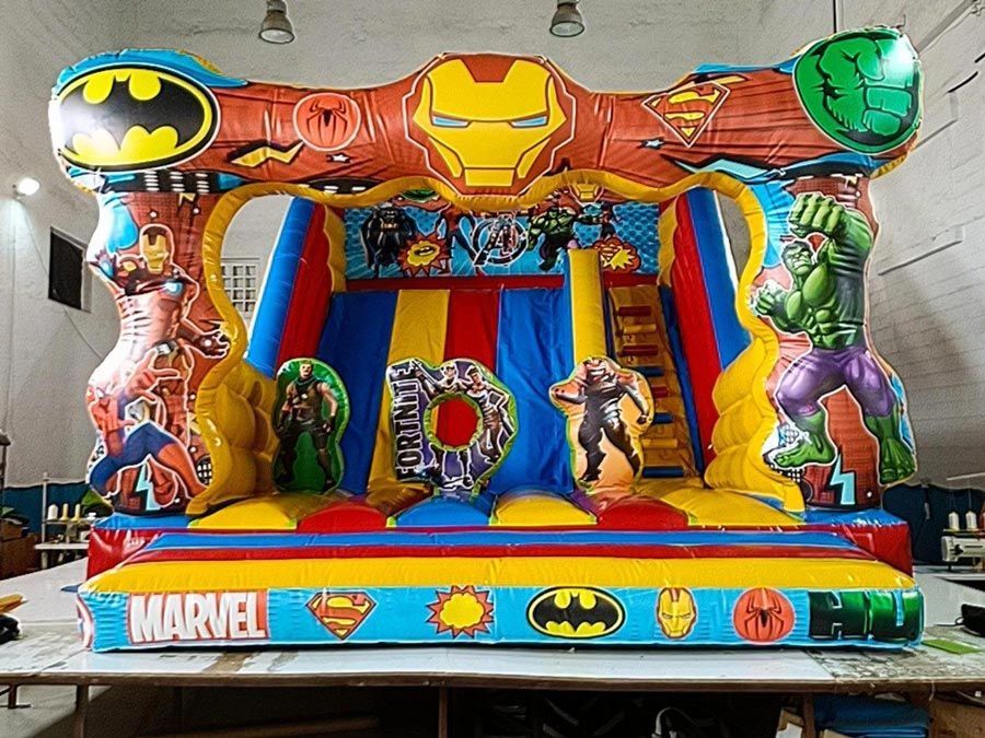 Colorida casa inflable con superhéroes de Marvel y DC, incluidos Iron Man, Batman y Hulk, con tobogán y zona de rebote.
