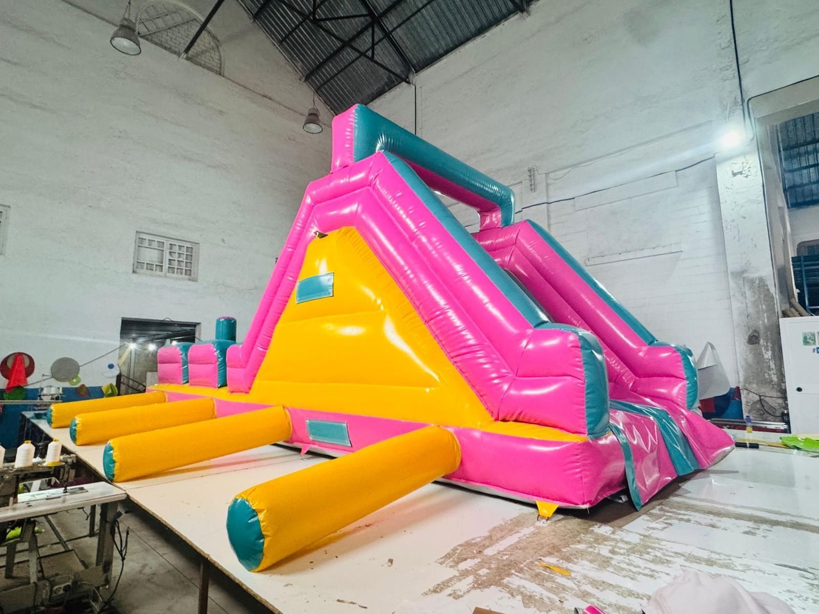 Un tobogán inflable rosa y amarillo está sobre una mesa en un almacén.