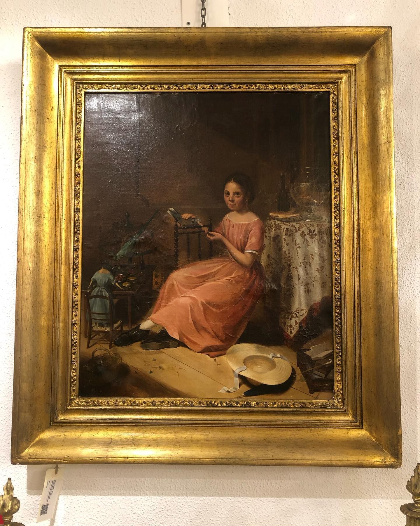 Pintura de uma pessoa vestida de rosa, sentada, segurando penas. Moldura dourada, ambiente interno.