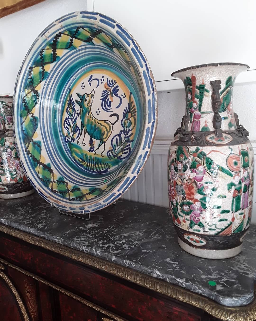 Um prato e um vaso de cerâmica decorados, ambos com padrões coloridos, repousam sobre uma superfície escura.