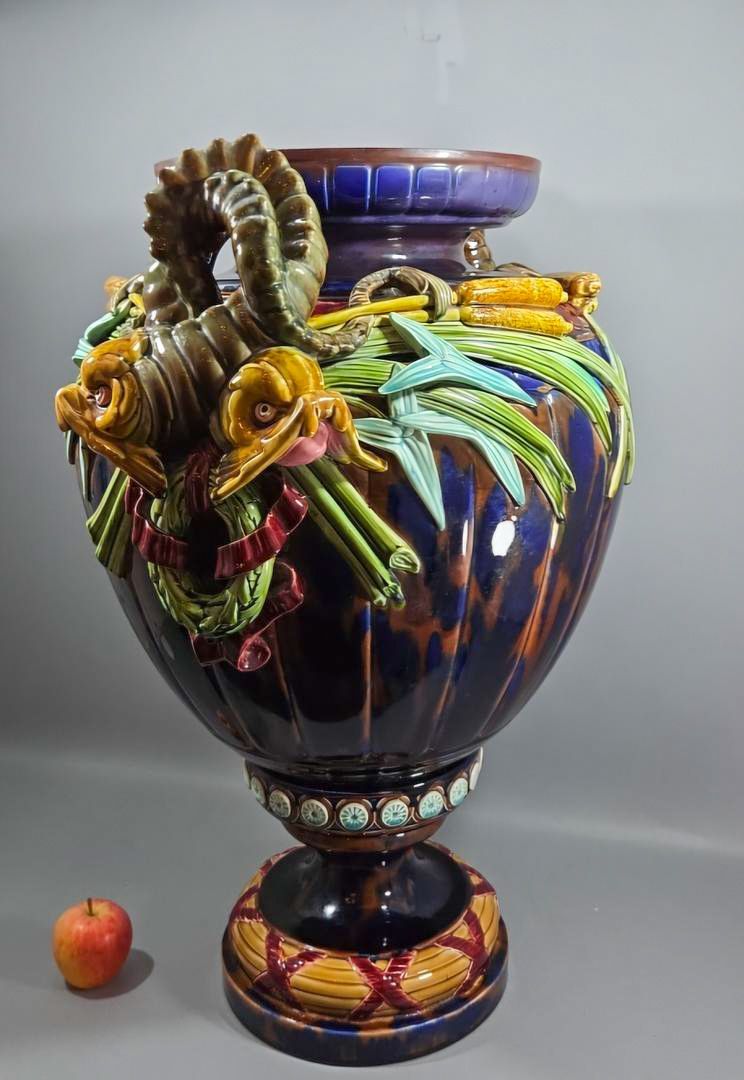 Vaso grande de cerâmica ornamentada, azul escuro com carneiro decorativo e detalhes coloridos sobre um pedestal.