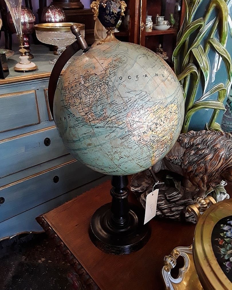 Globo terrestre antigo sobre suporte preto, com continentes em tons de verde-azulado e dourado, exposto em uma mesa .