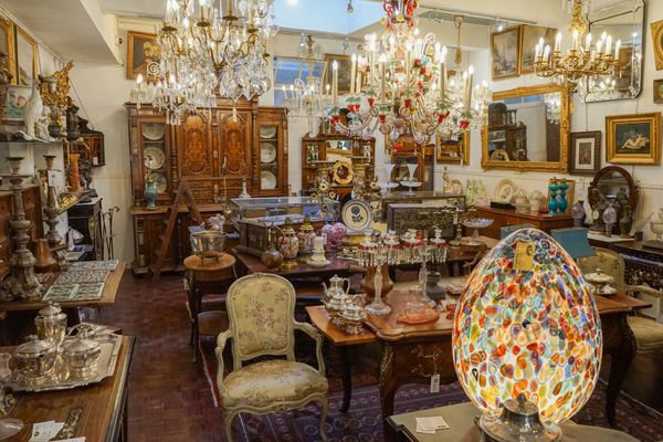 Interior de loja de antiguidades repleto de móveis, luminárias e objetos de decoração.