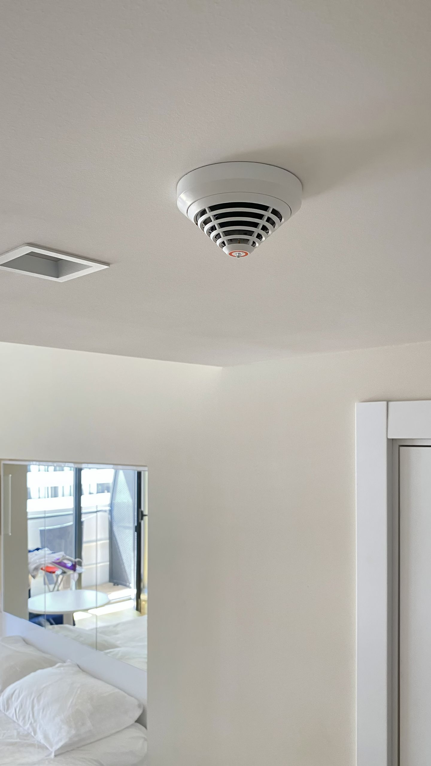 Détecteur de fumée fixé au plafond blanc avec une grille d'aération rectangulaire. Vue intérieure.