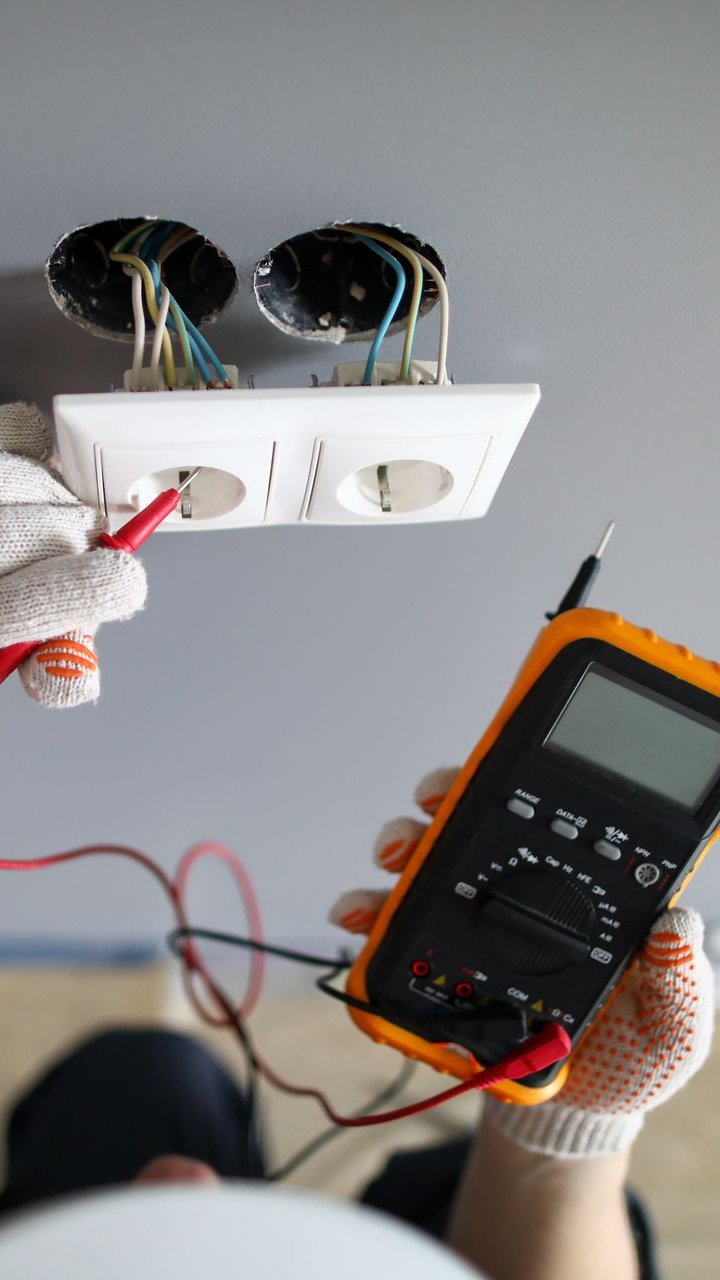 Une personne utilise un multimètre pour tester les fils d'une prise électrique, en portant des gants.