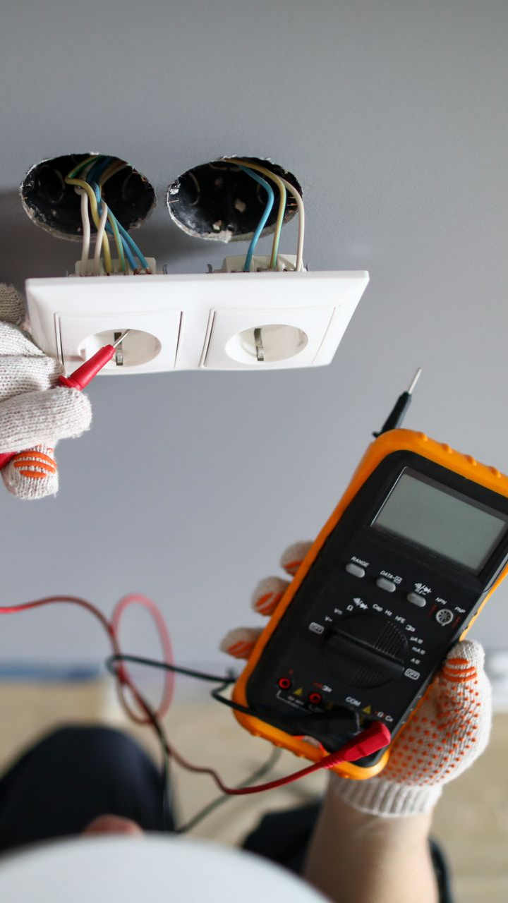 Un électricien teste une prise murale avec un multimètre, en portant des gants.