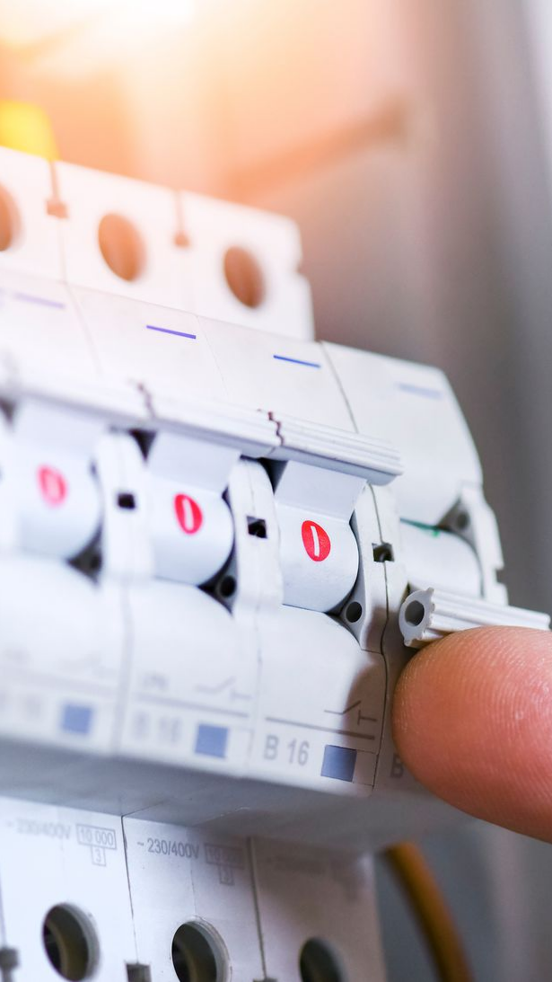 Doigt appuyant sur un interrupteur disjoncteur blanc dans un panneau.