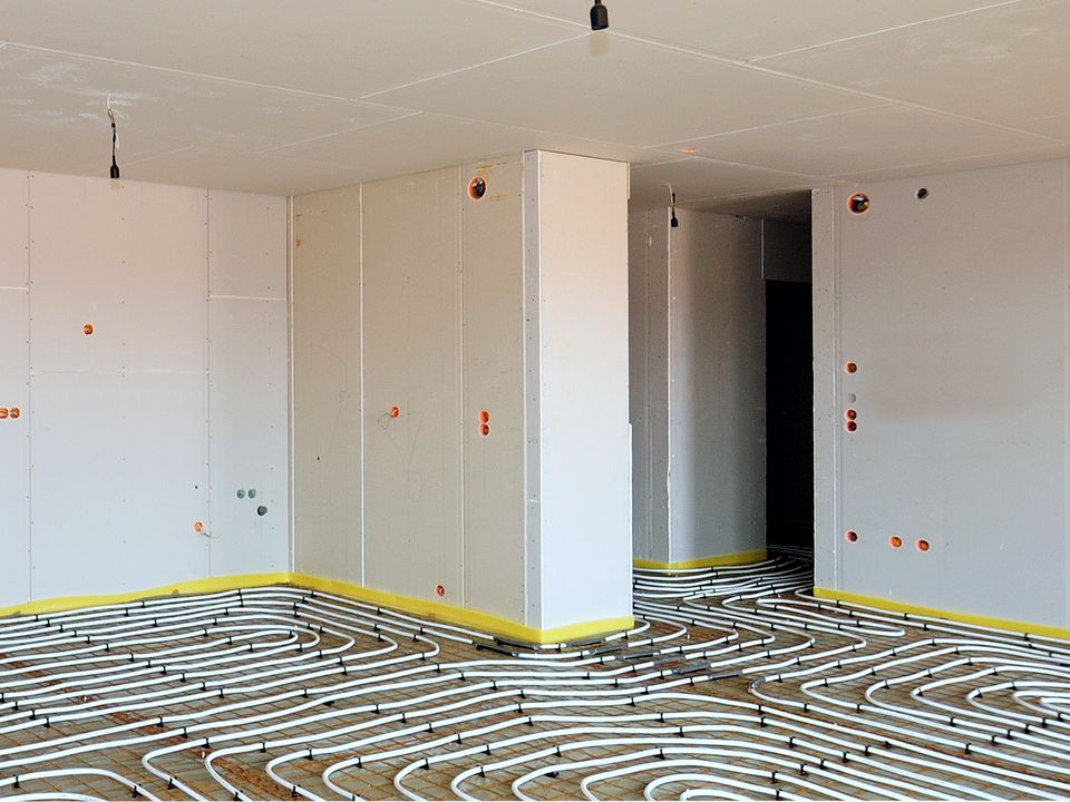 Pièce en travaux, murs et plafond blancs, système de chauffage au sol radiant apparent.