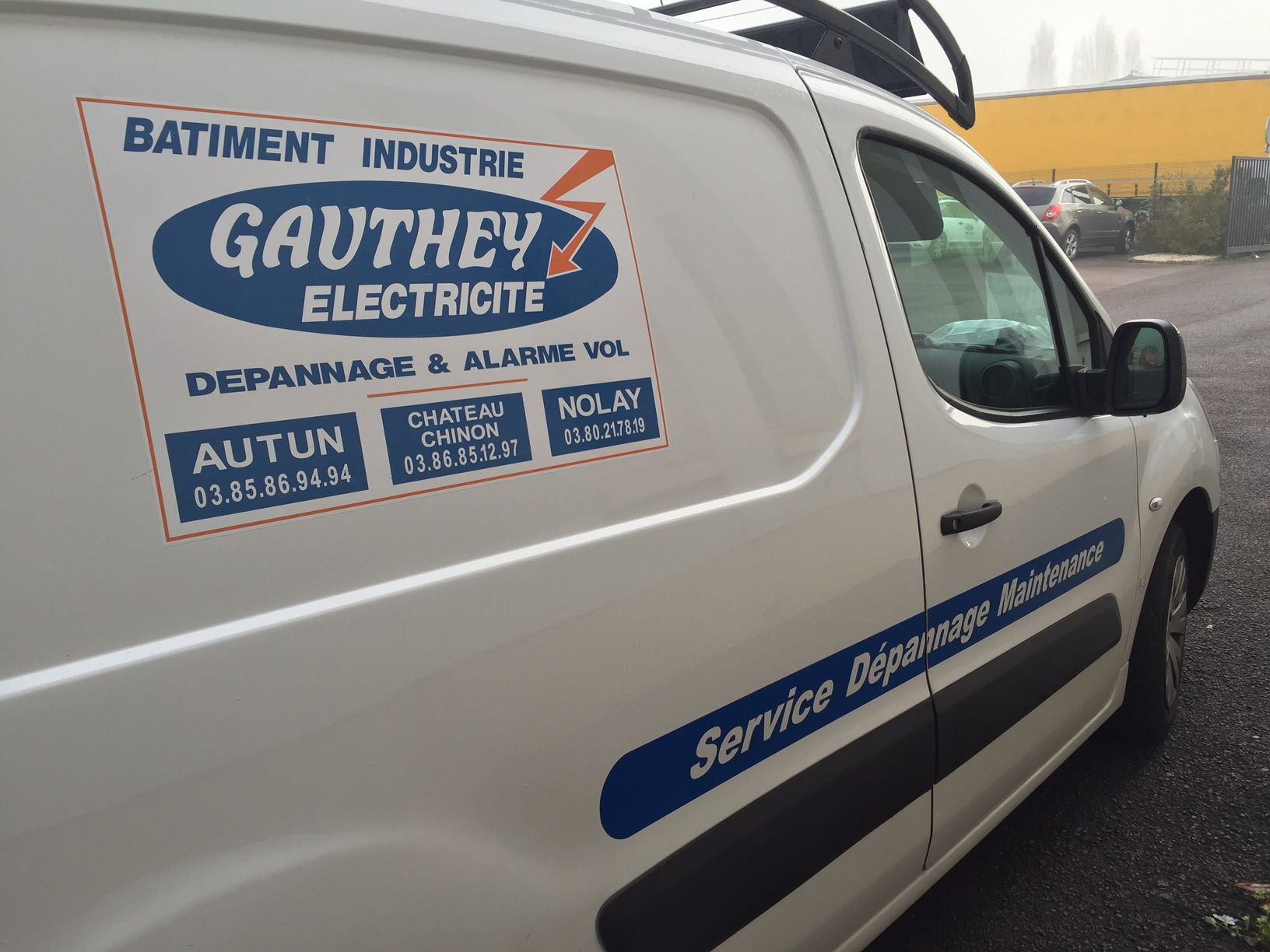 Camionnette blanche avec le logo « Gauthey Electricite » et les informations de service en bleu, stationnée à l'extérieur.