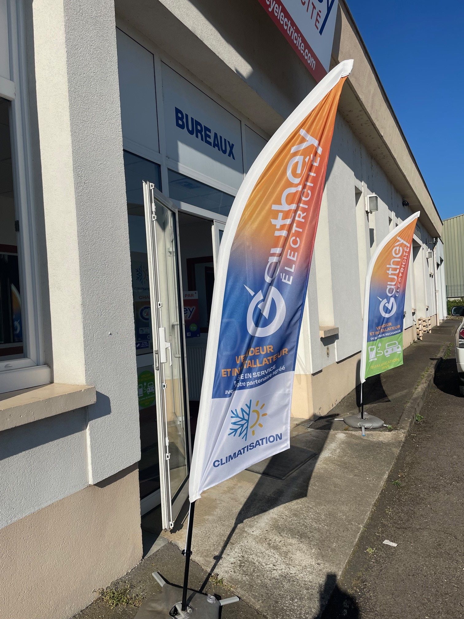 Un stand faisant la promotion de la recharge des véhicules électriques. Bannière avec logo. Borne de recharge fixée au mur, panneau vert.