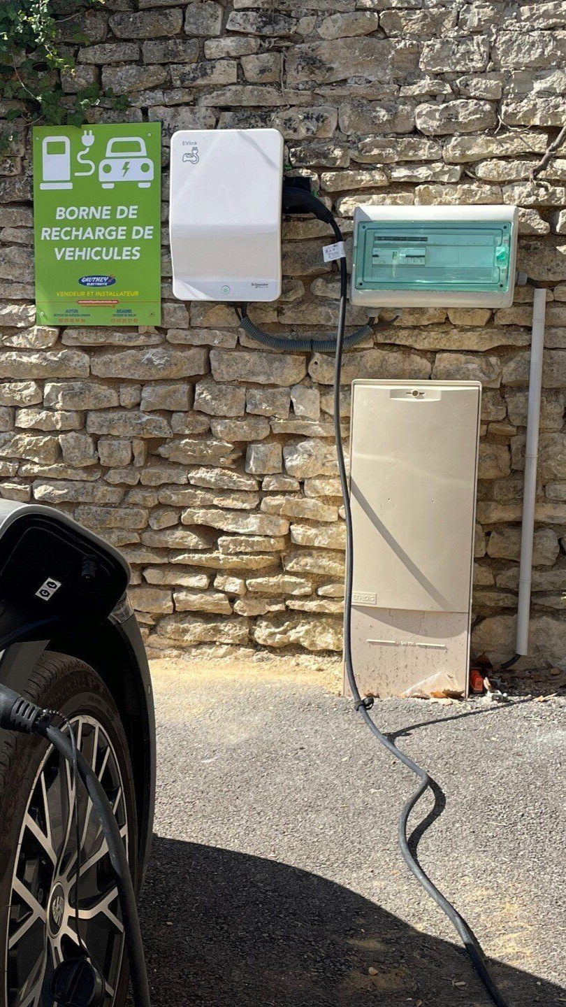 Une voiture électrique se recharge à une borne fixée à un mur en pierre. La borne comprend l'équipement de recharge.