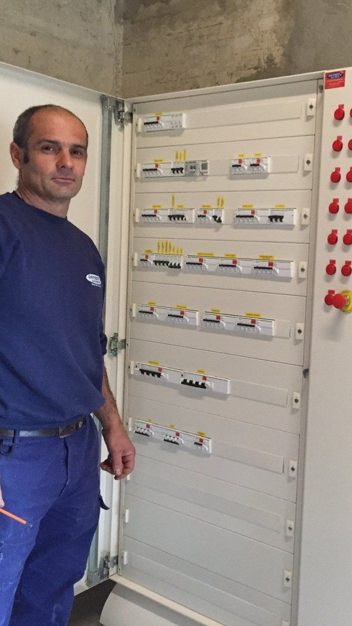 Un électricien se tient à côté d'un tableau électrique ouvert avec des disjoncteurs.