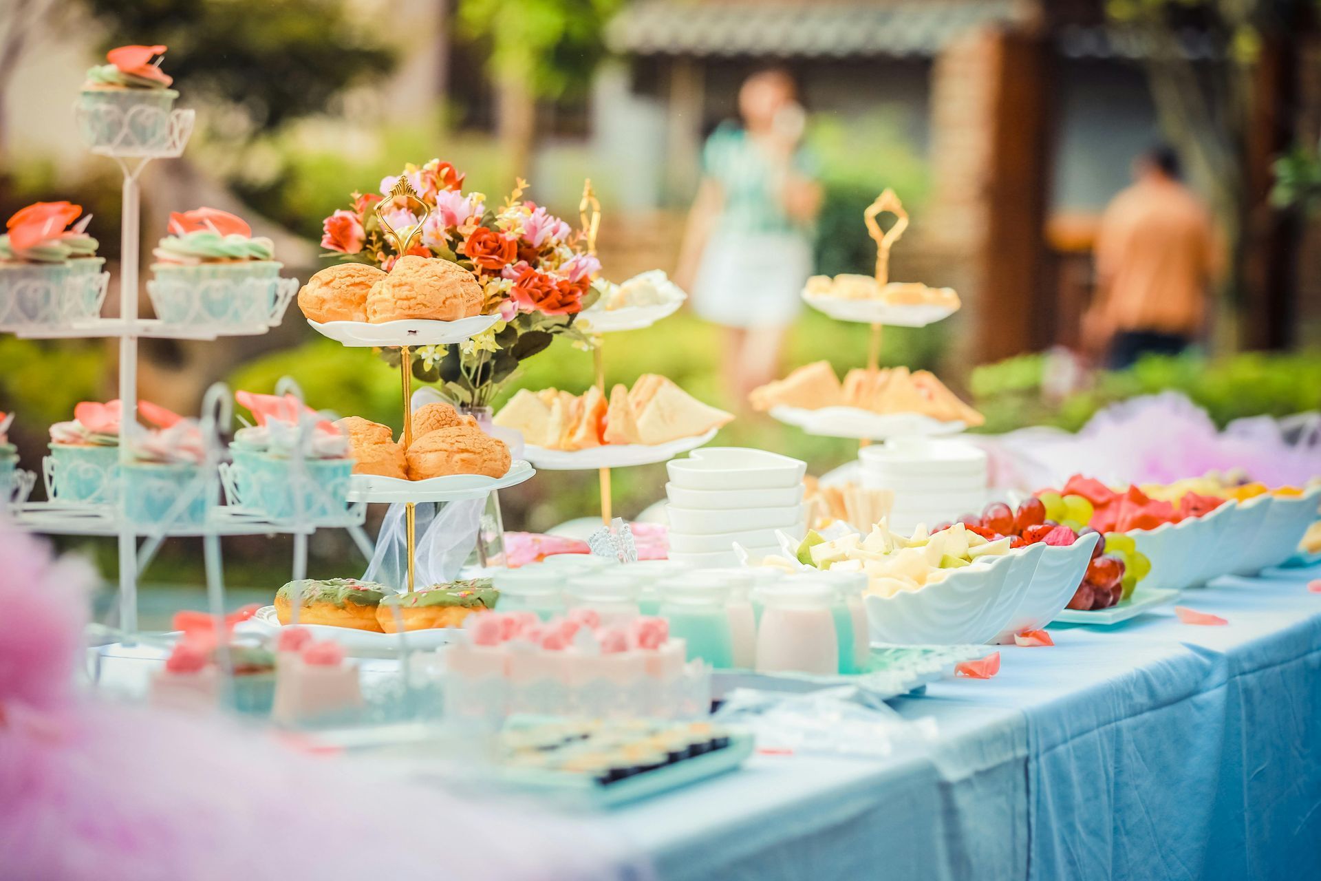 Una mesa de postres en un evento al aire libre, que incluye pasteles, bollería y sándwiches.