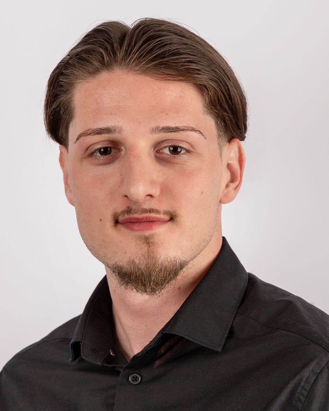 Ein junger Mann mit Bart trägt ein schwarzes Hemd.