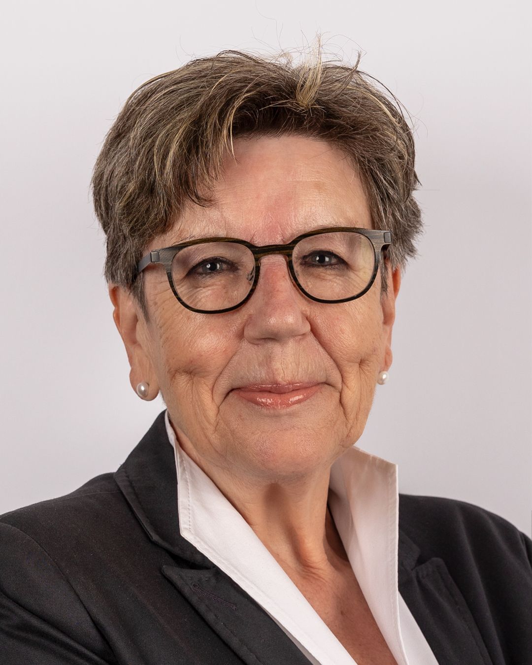 Eine Frau mit Brille und Anzug lächelt in die Kamera.