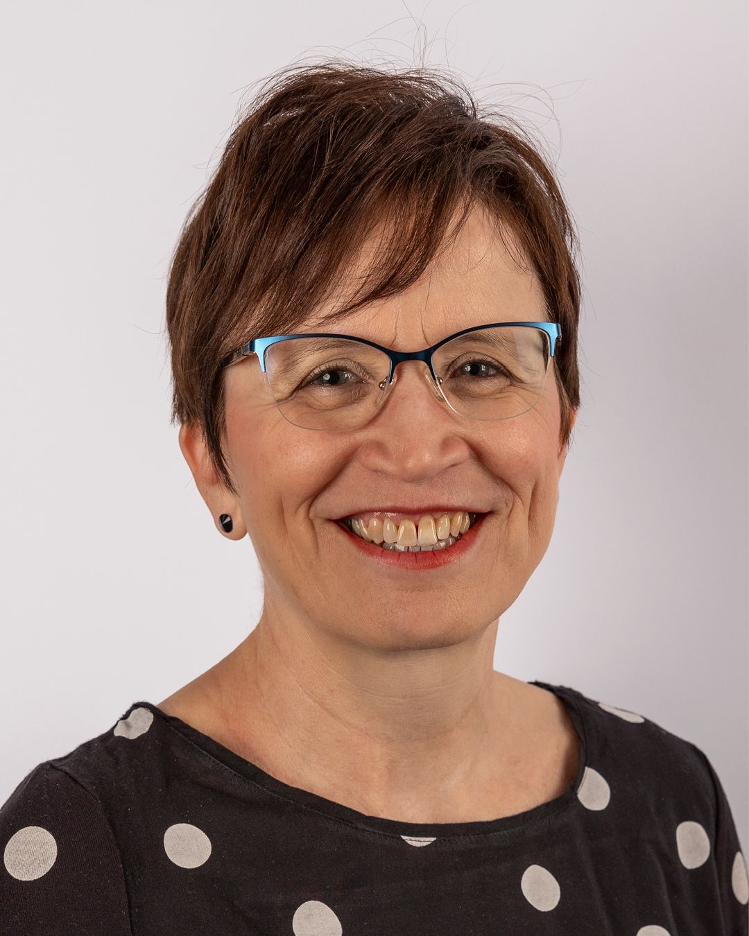 Eine Frau mit Brille und gepunktetem Hemd lächelt in die Kamera.