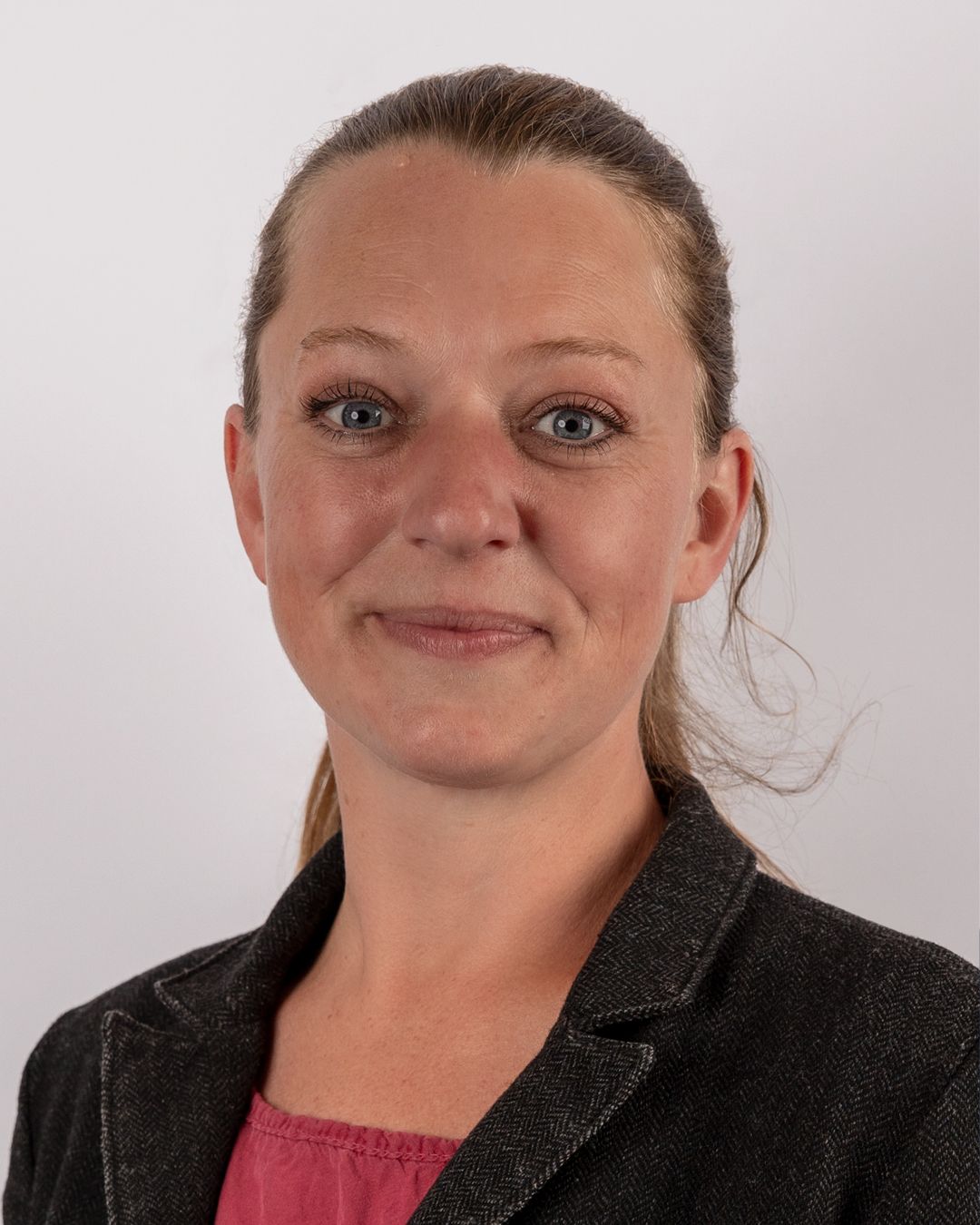 Eine Frau in einer schwarzen Jacke und einem rosa Hemd lächelt in die Kamera.