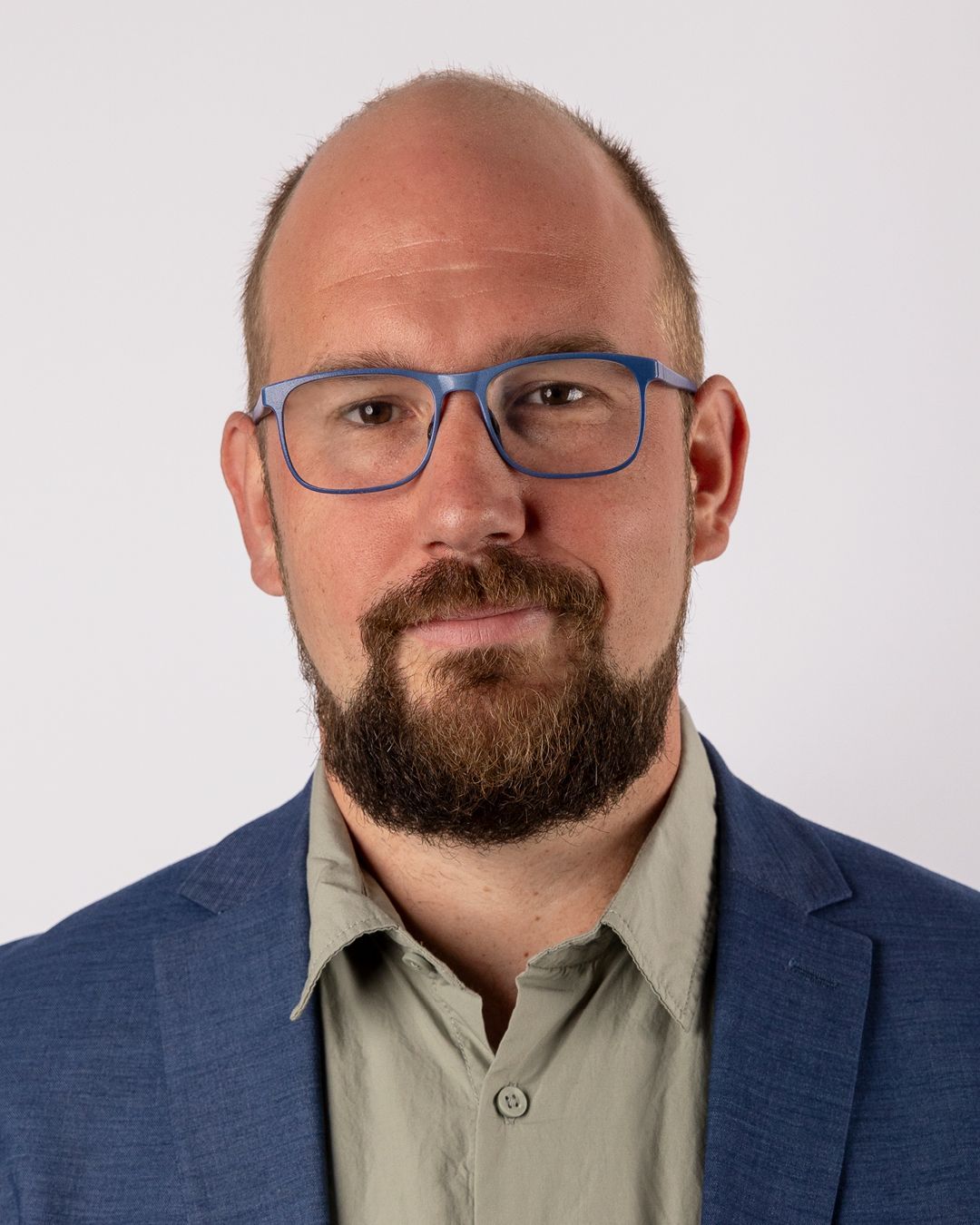 Ein kahlköpfiger Mann mit Bart, Brille und blauer Jacke.