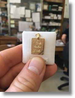 eine Person hält einen kleinen Goldanhänger in einer weißen Schachtel .