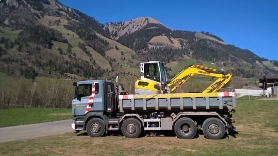 Un camion à benne basculante avec une excavatrice jaune attachée est garé devant une montagne.