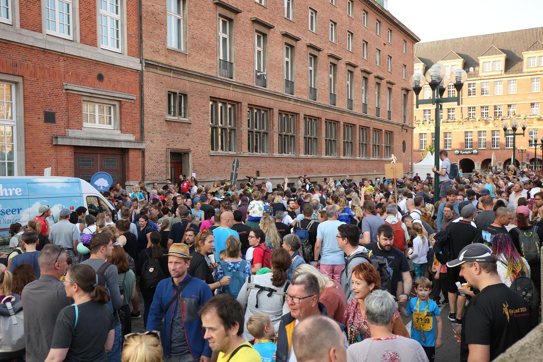 Ein überfülltes Straßenfest neben roten Backsteingebäuden, bei dem sich Menschen unter bunten Bannern und Zelten versammelt haben.