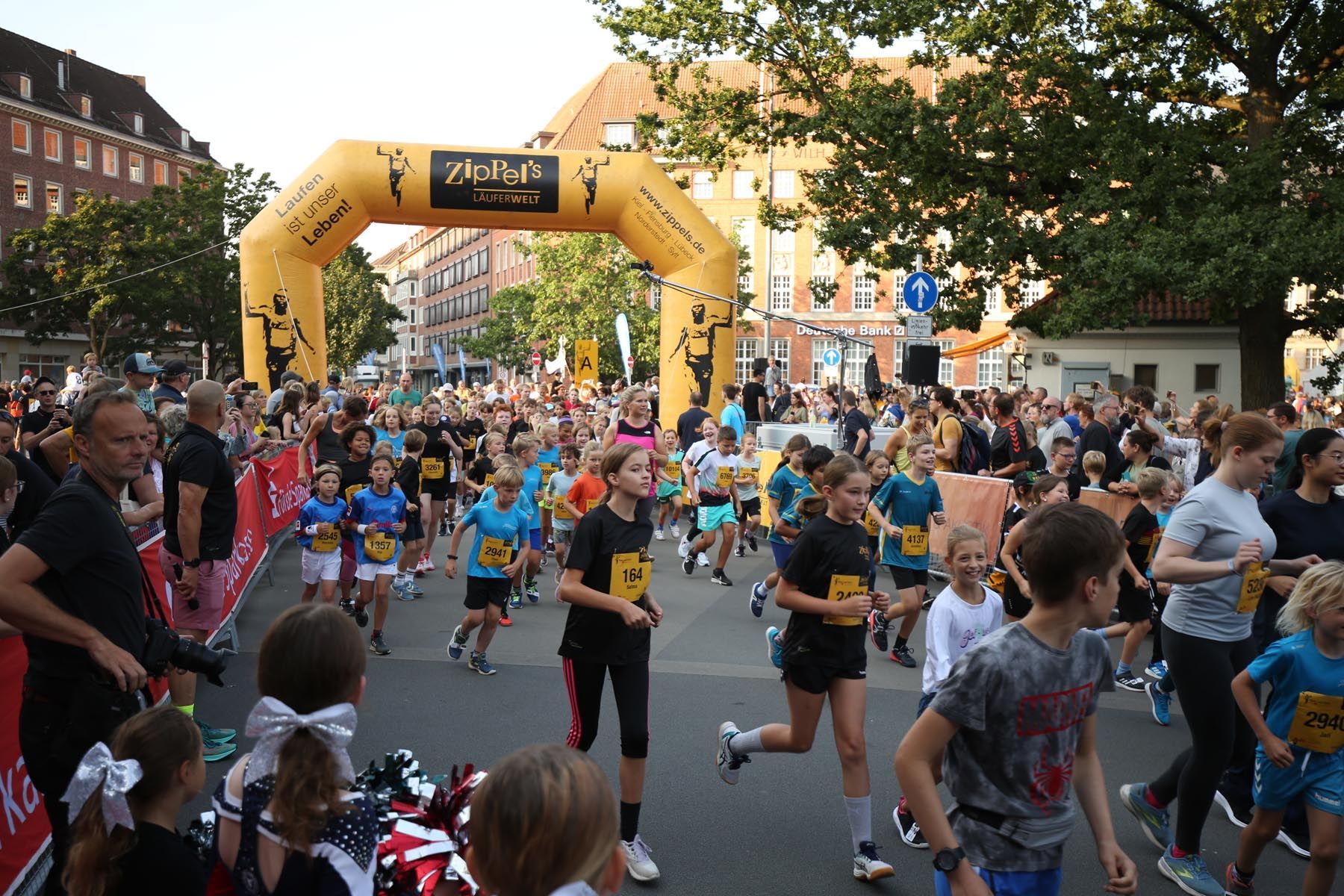 Ein überfüllter Stadtstraßenlauf, bei dem die Läufer unter einem gelben aufblasbaren Bogen in der Nähe der Ziellinie hindurchlaufen.