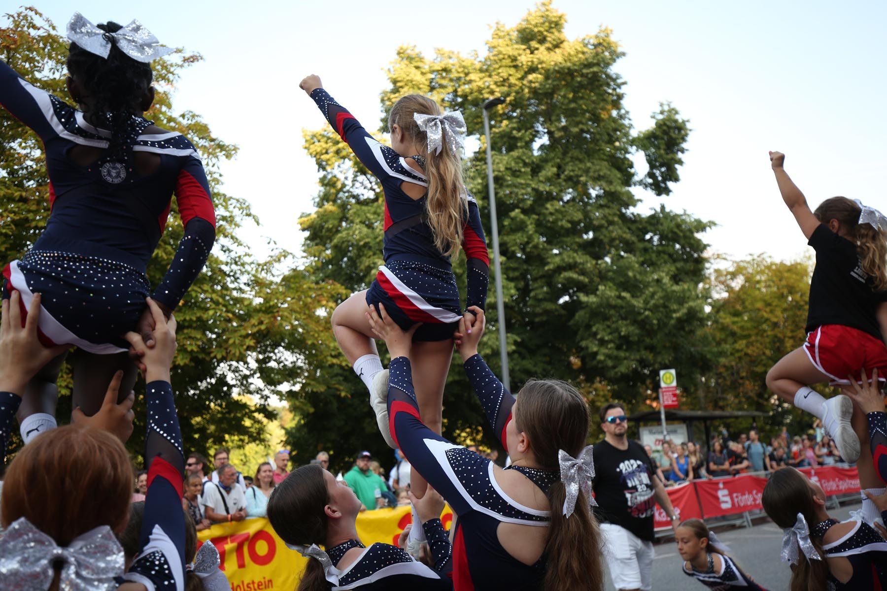 Cheerleader in marineblauen, roten und weißen Uniformen führen im Freien vor Publikum in einem Park Stunts vor.