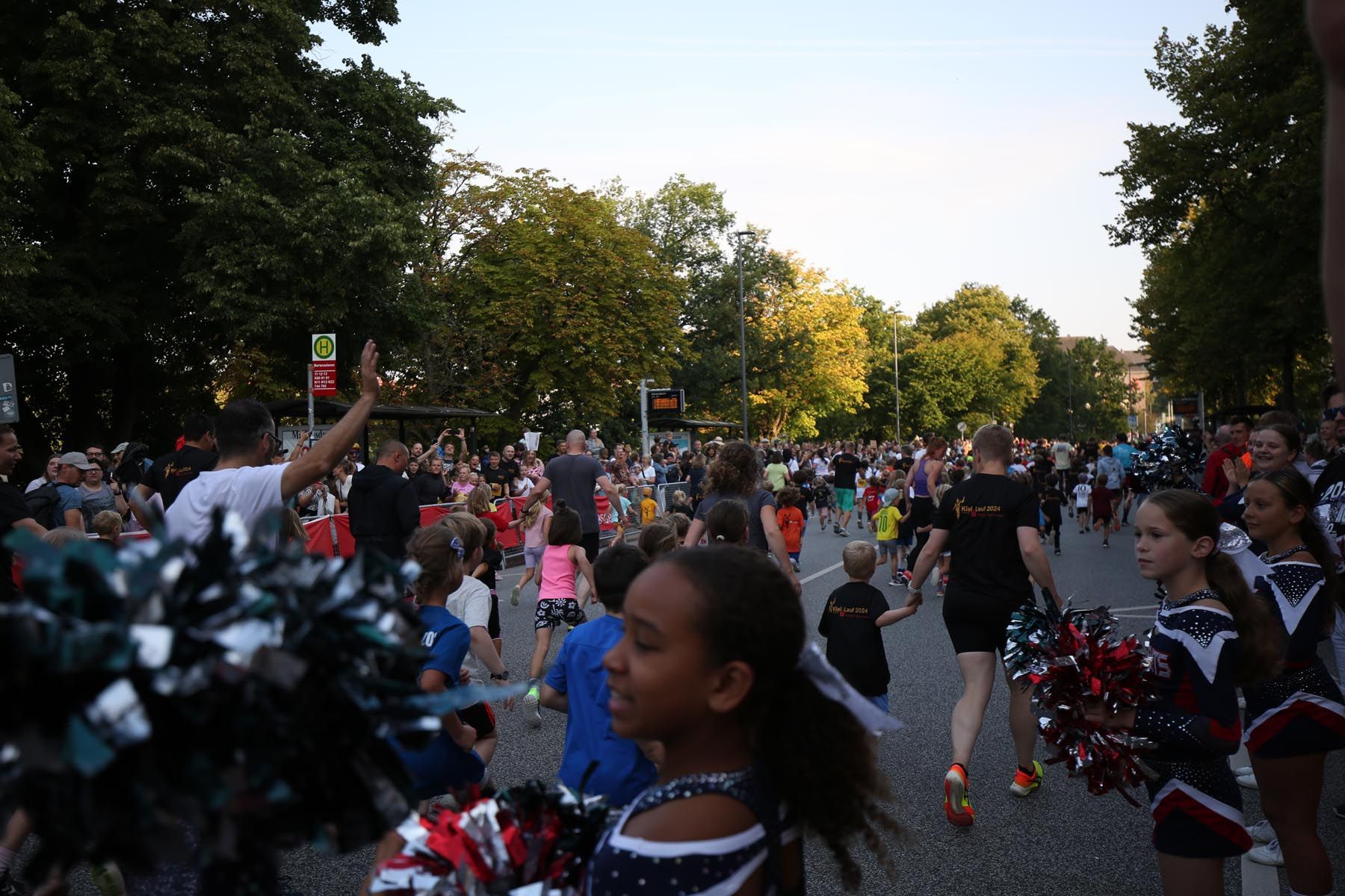 Menschenmenge bei einer Parade im Freien mit Cheerleadern und Konfetti in einem Park in der Abenddämmerung