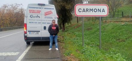 Persona de pie junto a una furgoneta blanca al lado de un cartel de carretera que dice “CARMONA”.