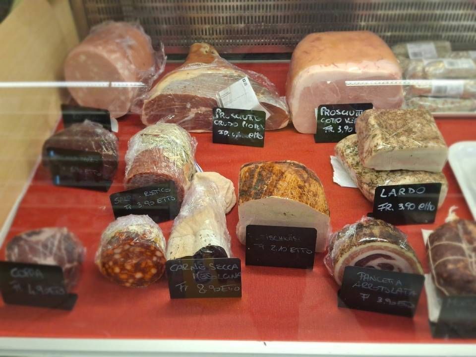 Una vetrina gastronomica con vari salumi ed etichette su una superficie rossa.