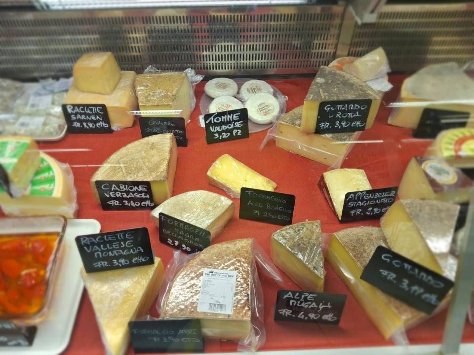 Vetrina con vari formaggi esposti su una superficie rossa. Le etichette nere indicano tipologie e prezzi.