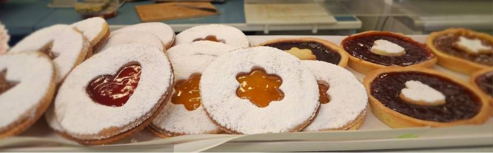 Biscotti e crostate, zucchero a velo, ripieno a forma di cuore e fiore, esposti su un vassoio.