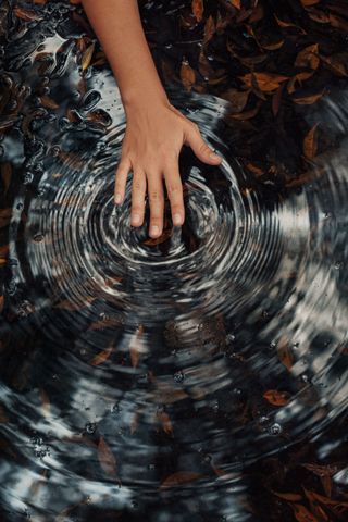 Remuant l'eau à la main dans une piscine sombre, créant des ondulations circulaires et des reflets.