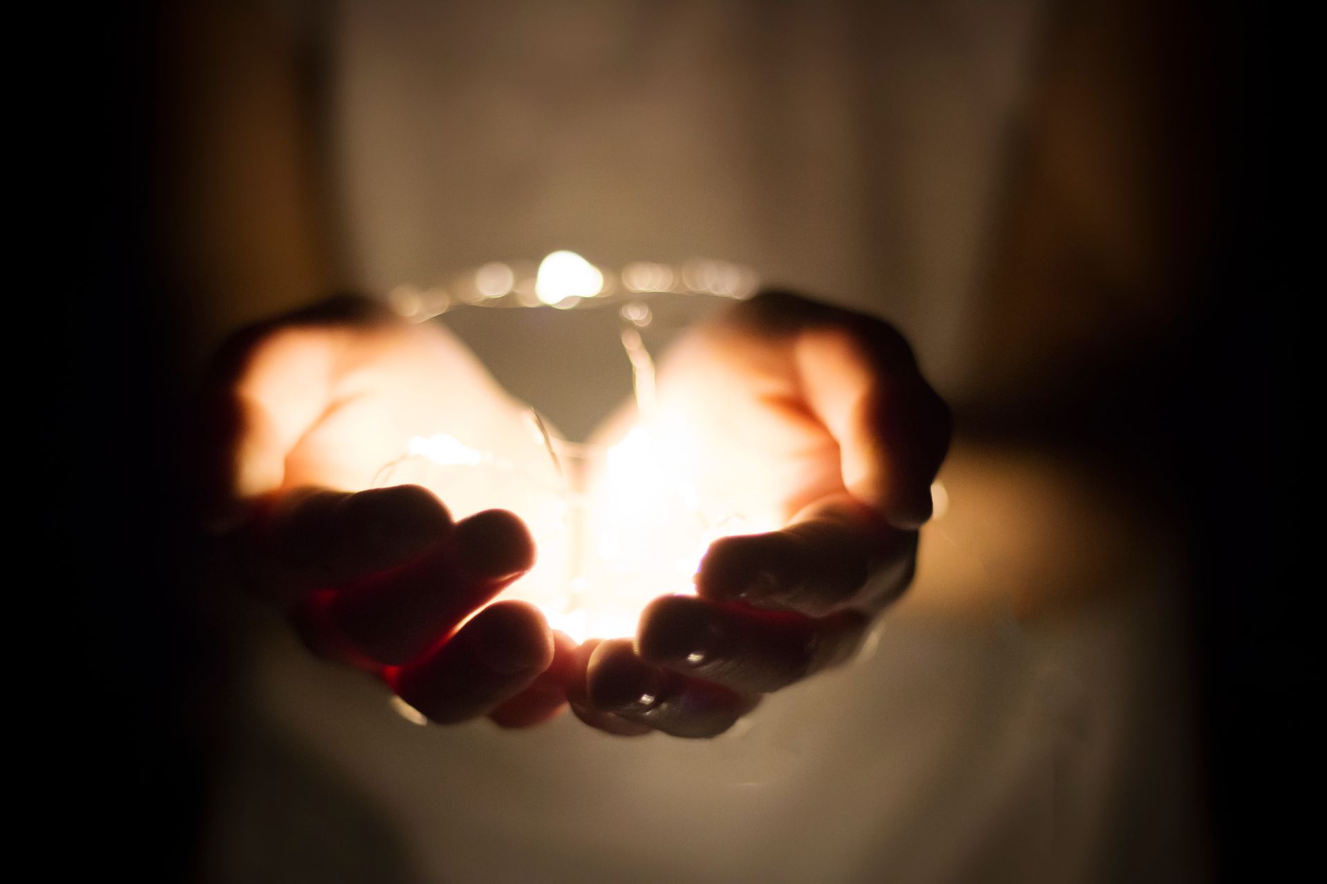 Des mains entourant une ampoule incandescente dans un environnement sombre