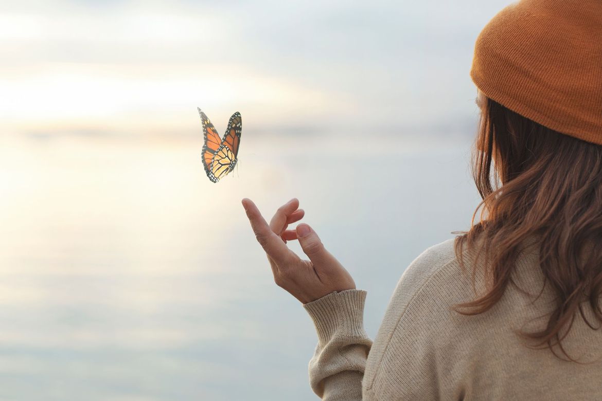 Femme tendant la main vers un papillon au-dessus d'une eau calme au coucher du soleil