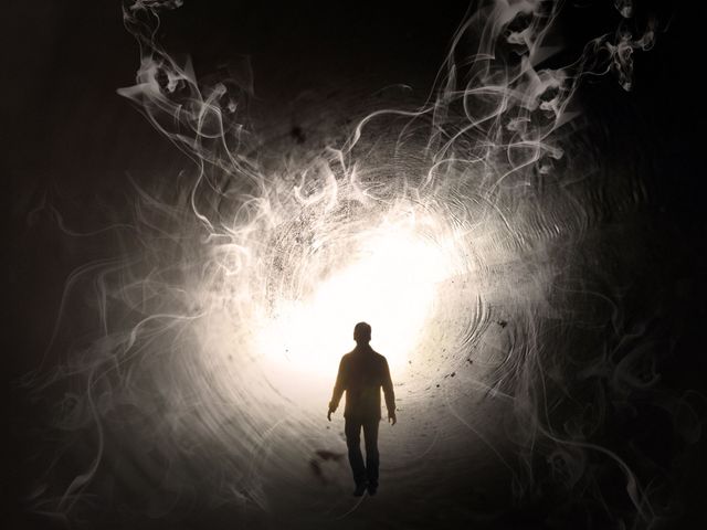 Silhouette d'une personne marchant vers une lumière blanche éclatante dans un tunnel sombre et enfumé