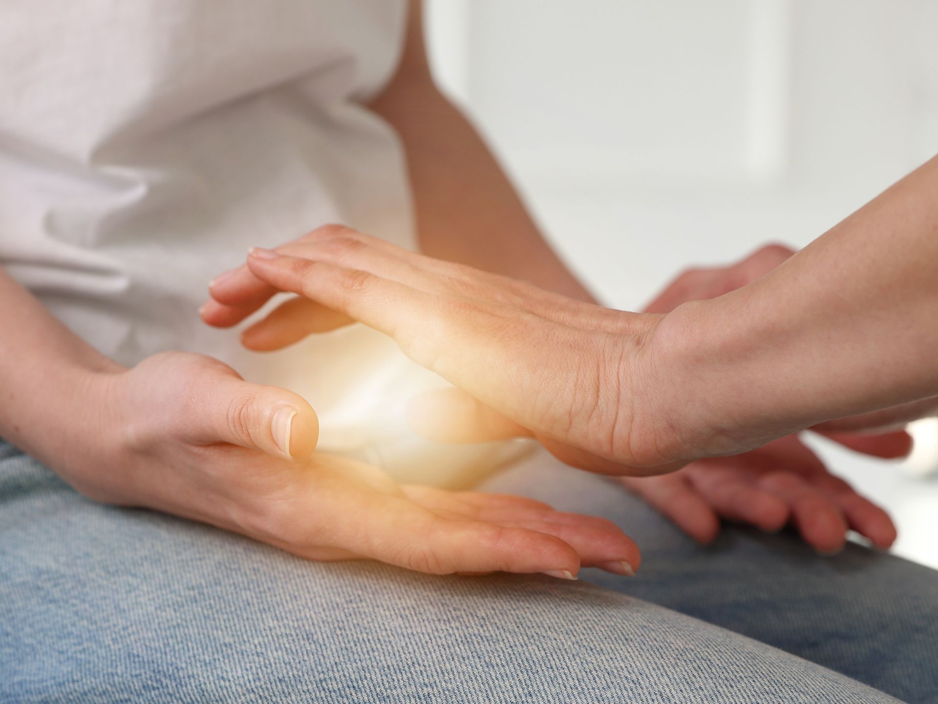 Des mains effleurent délicatement l'abdomen lumineux d'une personne assise, suggérant réconfort ou guérison.