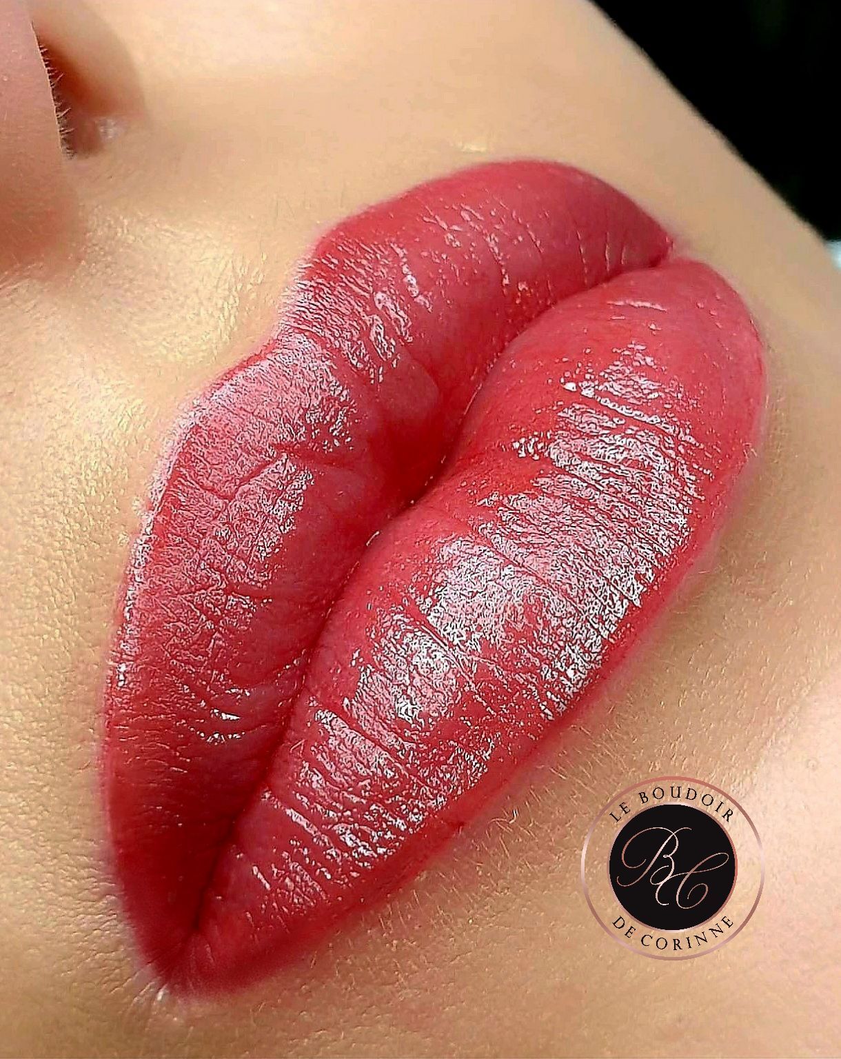 Lèvres rouges brillantes avec des reflets pailletés et un petit logo rond près du menton